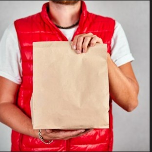 Entregador profissional vestindo colete vermelho e segurando uma sacola de papel pardo, representando a logística de um delivery de sucesso e a importância da experiência do cliente
